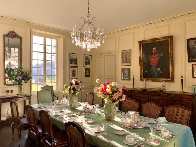 The panelled dining room laid for a meal beneath a crystal chandelier, hung with family portraits