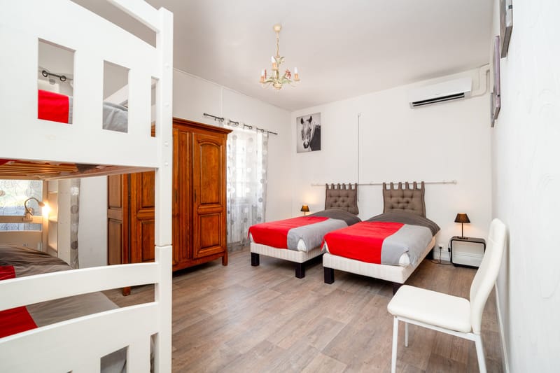 A bedroom in the Les Lauriers Roses gite with two single beds, a white bunk bed, a wooden wardrobe and a small chandelier.