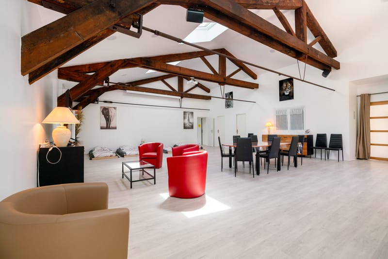 Open-plan lounge with exposed timber roof beams, red armchairs and a large dining table.