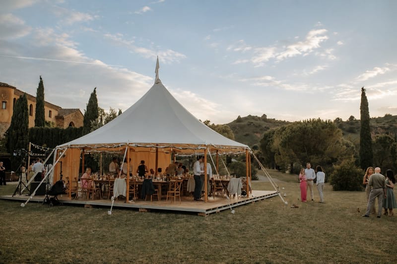 Sailcloth marquee lit from within at dusk, guests dining inside and the hills beyond