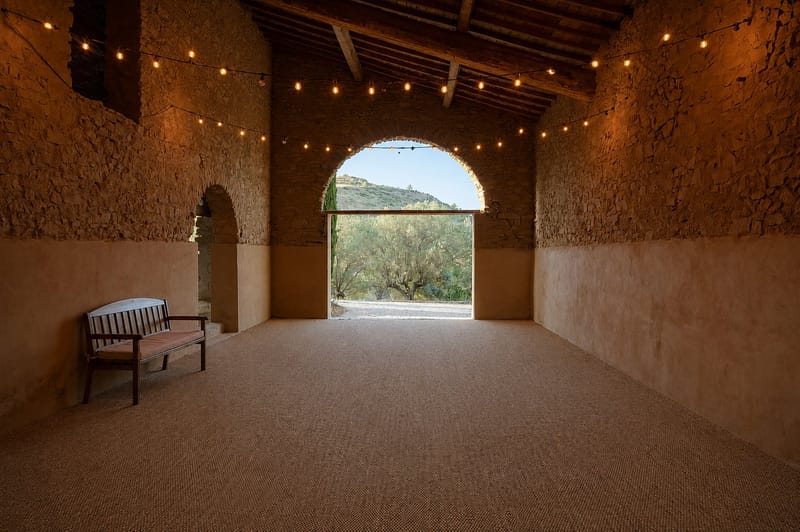Inside the barn, festoon lights and seagrass matting, the arched opening framing the olive grove