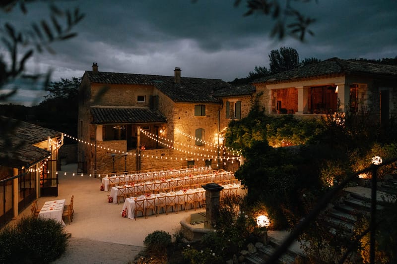 Courtyard long-table wedding dinner at dusk with festoon lights at Domaine de Valbonne