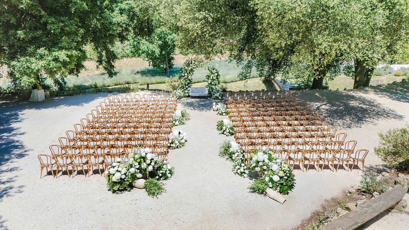 Aerial view of outdoor wedding ceremony with floral arch and wooden chairs at Domaine de Valbonne
