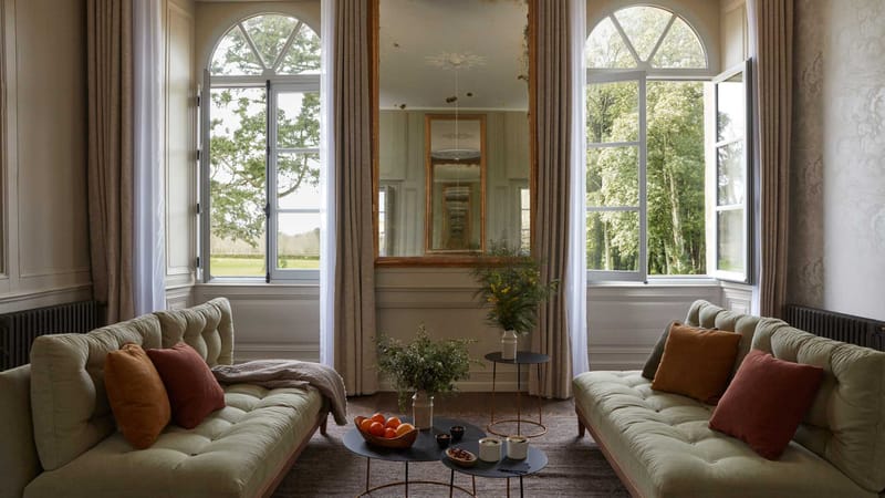 Salon in the chateau at Domaine Le Mezo with arched windows, a gilt mirror and linen sofas