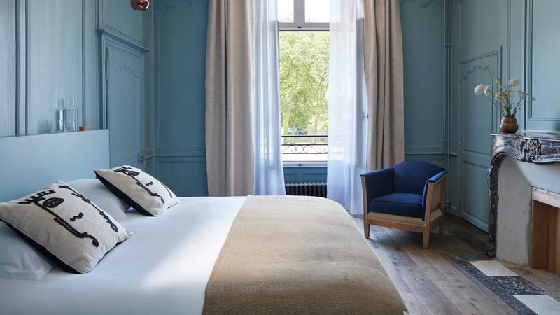 Bedroom in the chateau at Domaine Le Mezo with blue panelled walls, a marble fireplace and park views