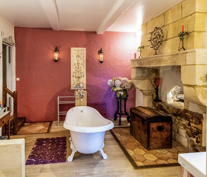 A bathroom with a freestanding bath in front of a stone fireplace and a rose-pink wall