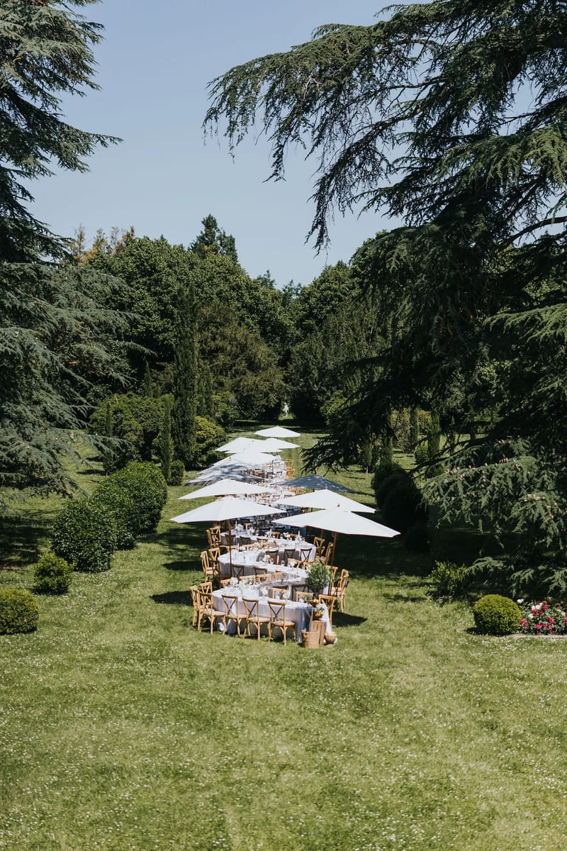Long table dinner under white parasols on the lawn, seen from above