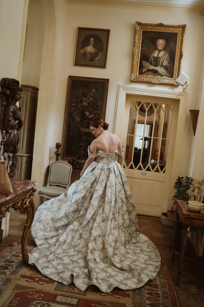 Panelled hall hung with portraits, a bride in a floral gown beside the door