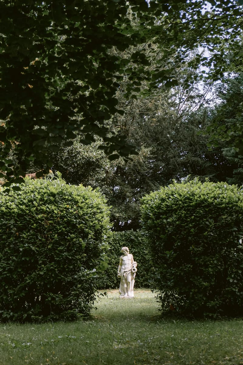 Stone statue on a clipped lawn framed by trees in the park