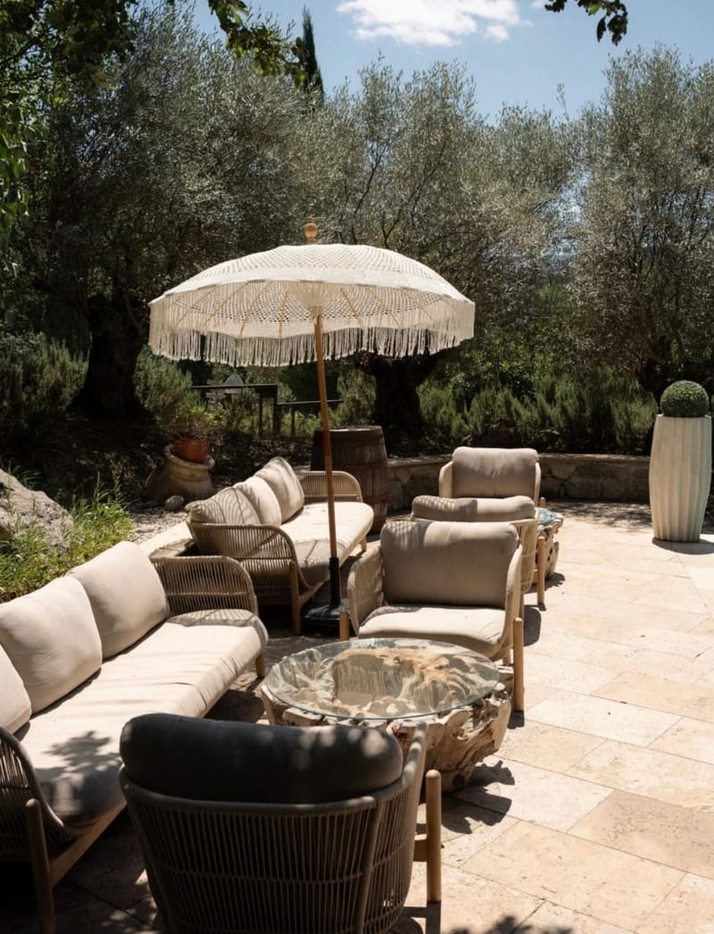 Outdoor lounge seating under a fringed parasol among the olive trees on the terrace at Le Mas des Cinq Fontaines.