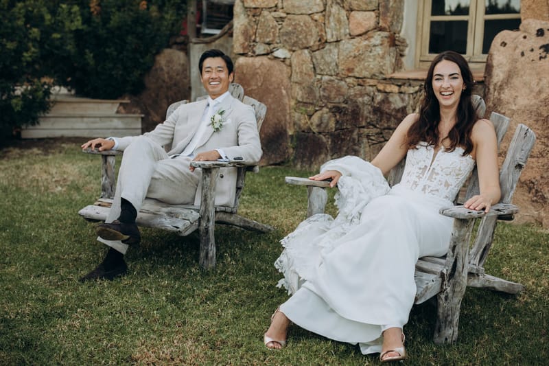 Couple seated on the lawn in front of the stone buildings at Les Oliviers de Palombaggia
