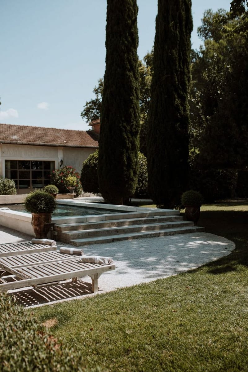 Mas D'Arvieux swimming pool with wooden loungers, cypress trees, and stone farmhouse in Provence