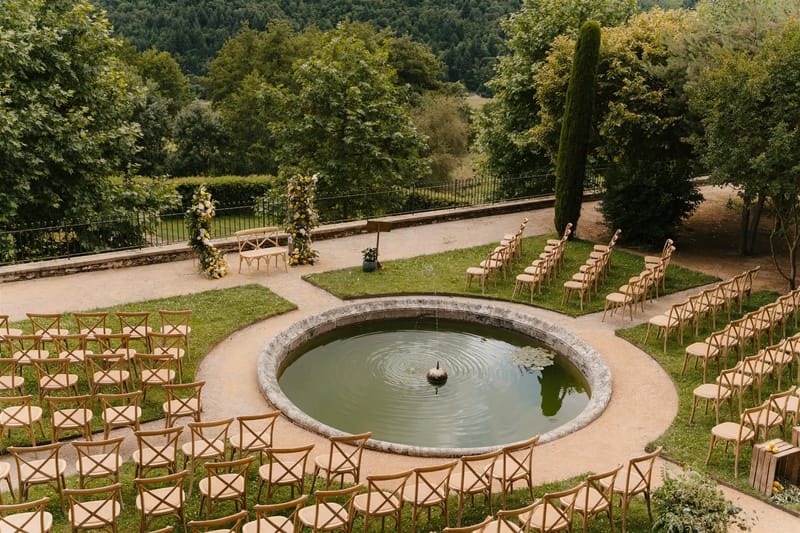 Outdoor wedding ceremony set around the round ornamental basin at Domaine de Vavril, with rows of white chairs and terraced gardens