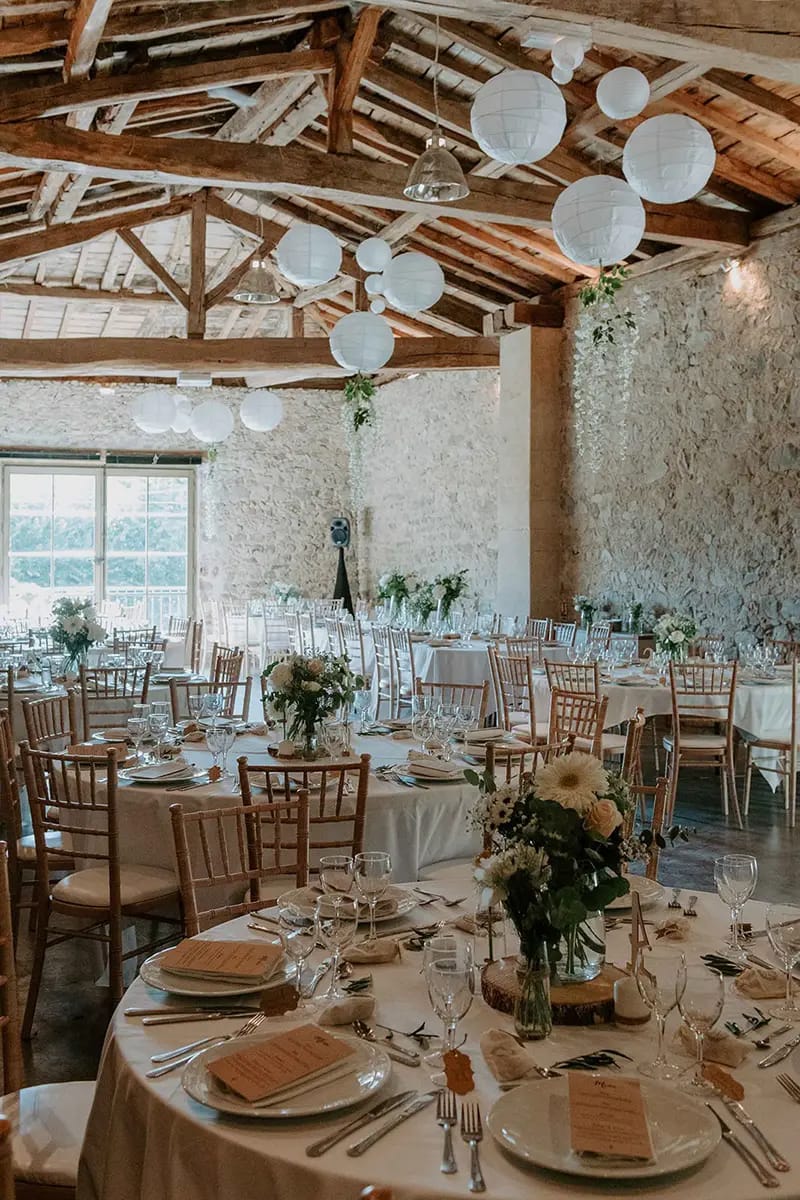 Wedding reception in the stone barn at Domaine de Vavril with tall floral centrepieces and hanging paper lanterns