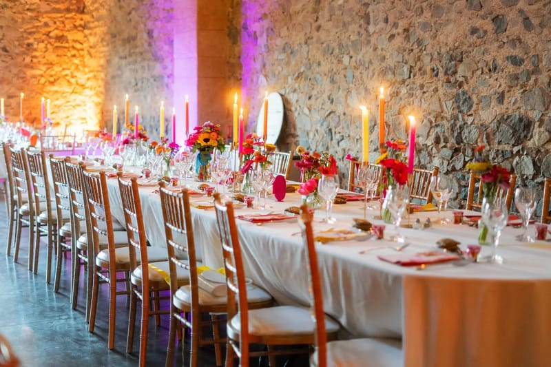 Long wedding table with red flowers and candlelight against the stone walls of the reception room at Domaine de Vavril