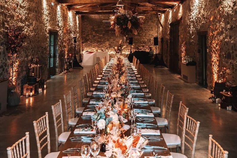 Evening wedding dinner on long tables in the stone barn at Domaine de Vavril, lit by candles and festoon lights