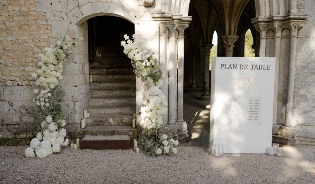 Abbaye Noce Machine sitting arrangement board outside reception white flower decor