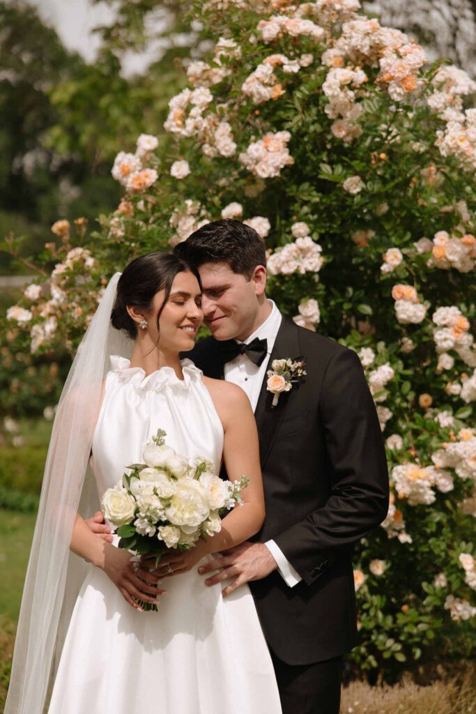 Boutonvillier F.Mary groom hugging bride from back bride holding bouquet flowers background