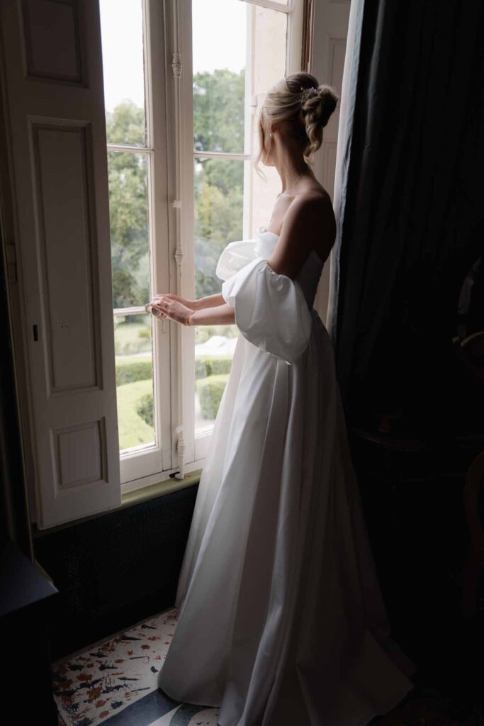 Chateau de Martinay Despinoy Wedding bride looking outside by window updo hair off shoulder dress