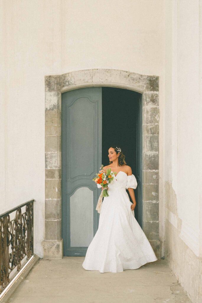 L Amour Fou 3 Maude C Photographe bride walking out door holding colorful bouquet