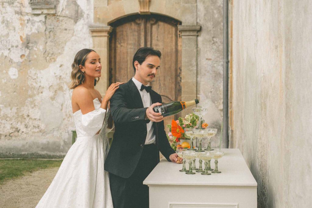 L Amour Fou 3 Maude C Photographe groom pouring champagne tower bride at the back