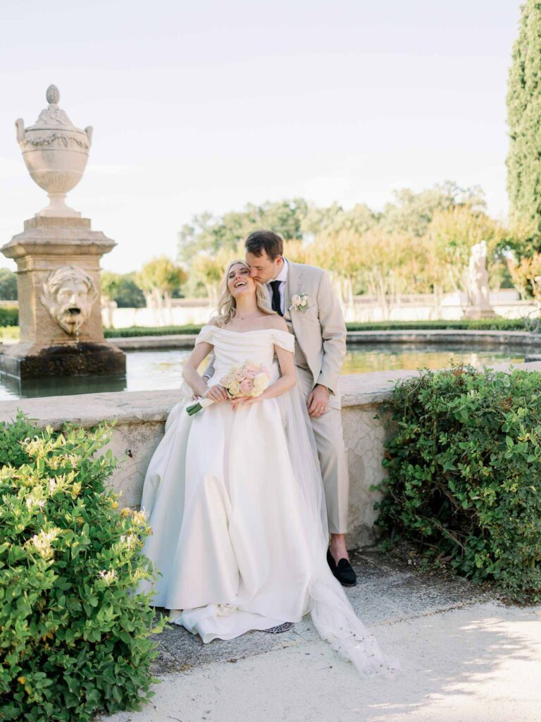 g.dominic m.marechal groom kissing brides cheeks fountain background