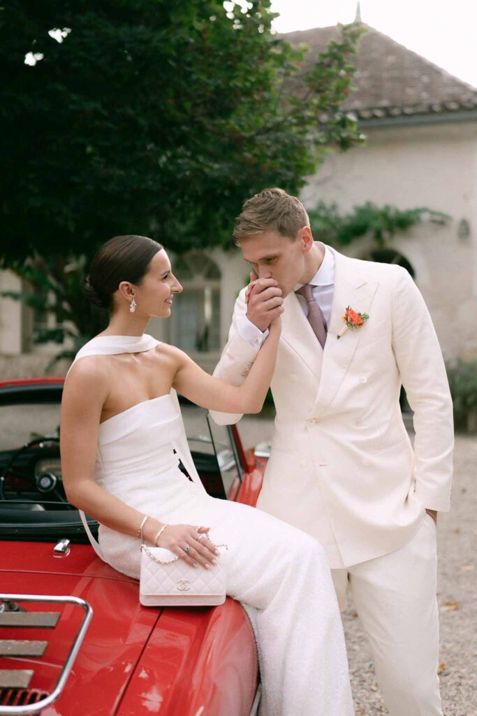 groom kissing bride hand on red vintage car